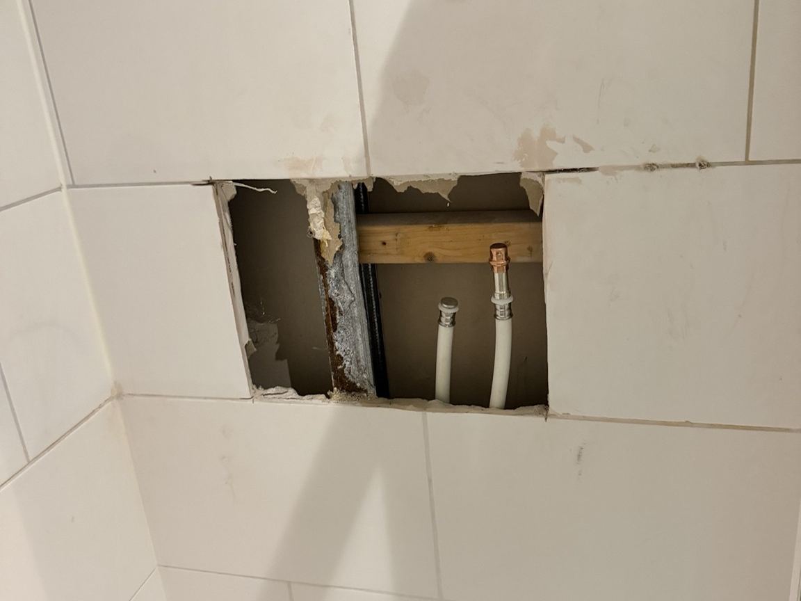 Geopende tegelwand bij een lekkende douche-aansluiting